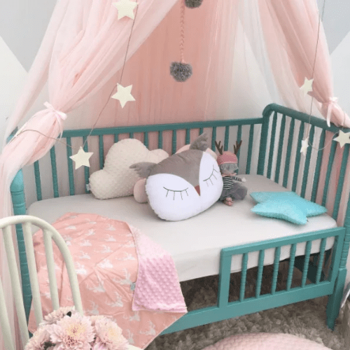 Ciel de Lit Bébé rose avec toile légère et décor étoiles au-dessus d'un lit bébé turquoise avec coussins peluche pour un espace sommeil cosy et protégé.