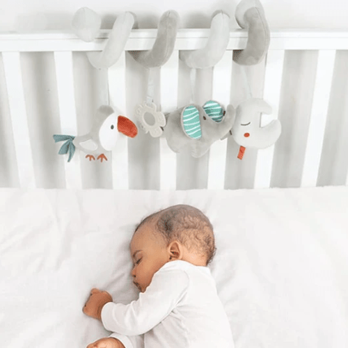 Hochet bébé suspendu avec jouets animaux doux au-dessus d'un bébé dormant dans un lit bébé blanc
