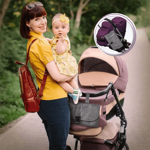 Sac matelas à langer nomade gris fixé à une poussette avec une maman tenant bébé en extérieur