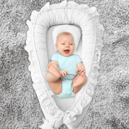 bébé souriant confortablement allongé dans un Nid de Cocon Bébé blanc aristocratique sur tapis gris doux