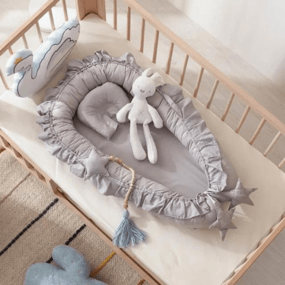 Nid de Cocon Bébé gris clair en coton doux avec design ergonomique et déco étoile dans un lit bébé en bois