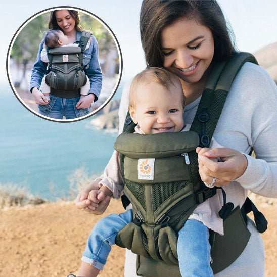 porte bébé ergonomique vert porté par une maman souriante avec bébé heureux devant un paysage côtier