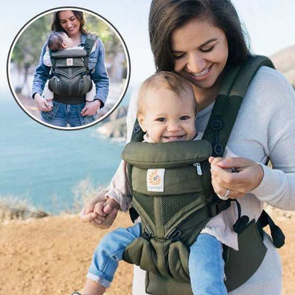porte bébé ergonomique vert porté par une maman souriante avec bébé heureux devant un paysage côtier