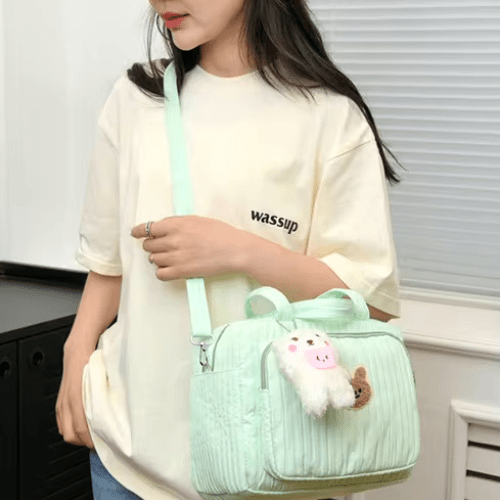 Sac à langer vert pastel avec motif dessin animé et peluche, porté par une femme en t-shirt crème, design léger et fonctionnel.