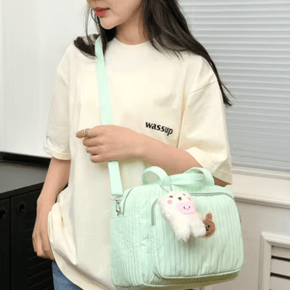 Sac à langer vert pastel avec motif dessin animé et peluche, porté par une femme en t-shirt crème, design léger et fonctionnel.